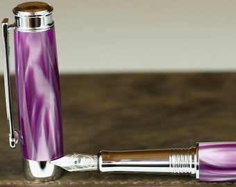 May include: A purple and white swirl fountain pen with a silver cap and nib. The pen is lying on a brown leather-bound journal.