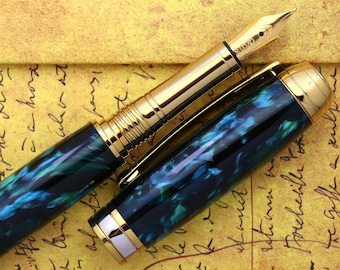 Könnte beinhalten: Ein schwarzer und grüner Füllfederhalter mit goldenen Akzenten und einer feinen Feder. Der Stift liegt auf einem Stück vergilbtem Papier mit handschriftlichem Text.