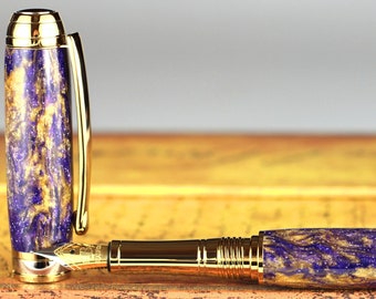 Könnte beinhalten: Ein luxuriöser Füllfederhalter mit goldfarbenem Clip und Feder. Der Schaft und die Kappe des Stifts weisen ein wirbelndes Muster aus Lila und Gold auf. Der Stift liegt auf einer Holzoberfläche.