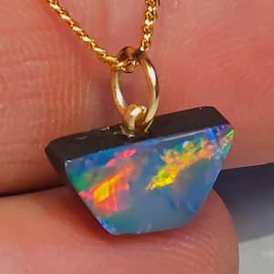 May include: A gold chain necklace with an opal pendant. The opal displays a dark base with flashes of yellow, orange, and blue. The pendant is attached to the chain with a gold bail. The necklace is a piece of jewellery.