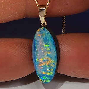 Op de afbeelding: Een gouden ketting met een hanger met een blauwe, groene en oranje opaal, gezet in een zwarte bezel.