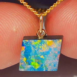 May include: A gold necklace with a pendant featuring a colourful opal stone. The opal displays shades of blue, green, and yellow. The pendant is a trapezoid shape with a dark border. The chain is a twisted rope design.