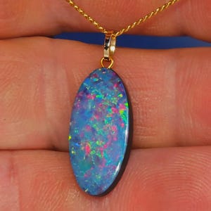 May include: A gold chain necklace with an oval pendant. The pendant features a vibrant opal with a blue base colour and flashes of pink, green, and yellow. The opal is set in a gold bezel.