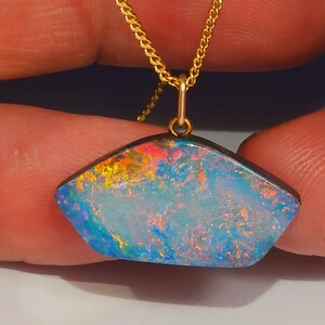 May include: A gold chain necklace with a pendant featuring a vibrant opal gemstone. The opal displays a spectrum of colours, including blue, pink, and yellow, set against a dark border. The pendant is held by a delicate gold bail.