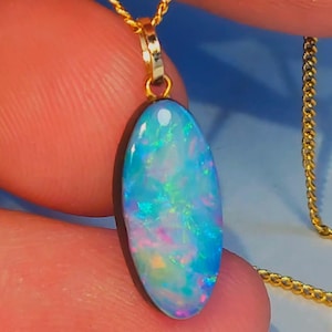 May include: A gold chain necklace with an oval opal pendant. The opal showcases a colourful play of light, with shades of blue, green, and pink. The pendant hangs from a fine gold chain.