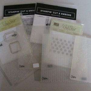 May include: A set of clear plastic embossing folders for use with a die-cutting machine. The folders feature various patterns, including a floral design, a geometric pattern, and a design with the text "Big Shot". The folders are labeled with the brand names "Cuttlebug" and "Sizzix".
