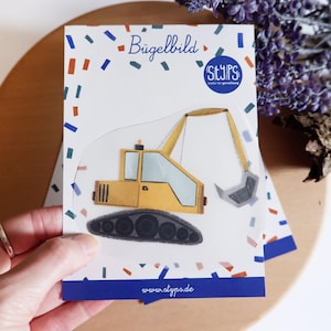 Könnte beinhalten: Ein gelb-grauer Aufbügler mit einem Cartoon-Bagger. Der Aufbügler trägt oben den Text "Bügelbild" und unten "www.atypo.de". Der Aufbügler befindet sich auf einem weißen Hintergrund mit blauen und roten Konfetti.