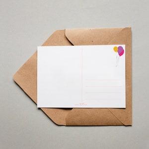 May include: A blank postcard with a brown envelope. The postcard has a light pink and purple balloon illustration in the top right corner.