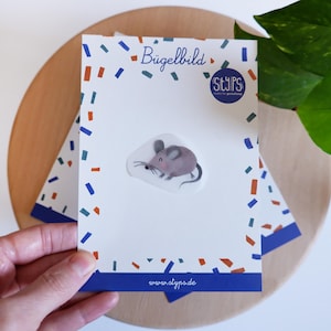 Könnte beinhalten: Eine weiße Karte mit einem Cartoon-Maus-Aufkleber, Konfetti und dem Text "Bügelbild". Die Karte hat einen blauen Rand und die Website www.alypa.de. Die Karte liegt auf einer Holzoberfläche.