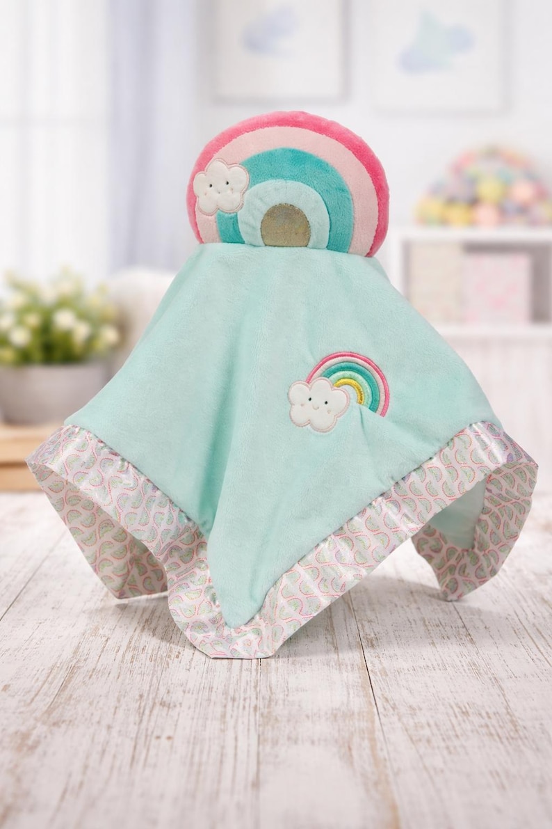 May include: A soft, mint green baby blanket with a rainbow and cloud design. The blanket has a satin trim with a pink and white pattern. A rainbow and cloud applique is on the blanket.