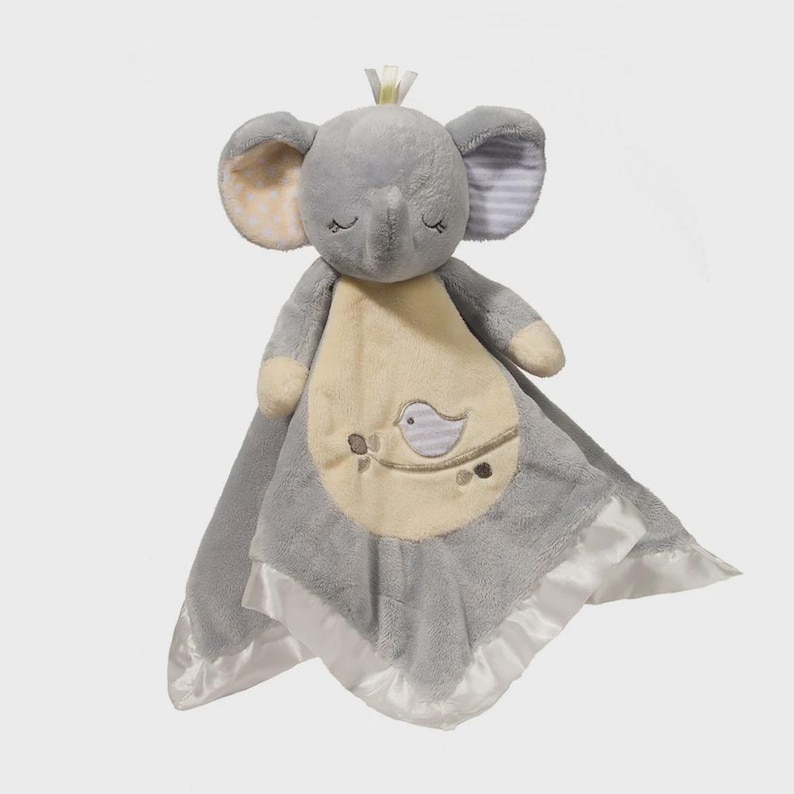 May include: A gray elephant-shaped baby security blanket with a cream-colored center and a bird design. The blanket has a satin border and a small crown on top of the elephant's head.