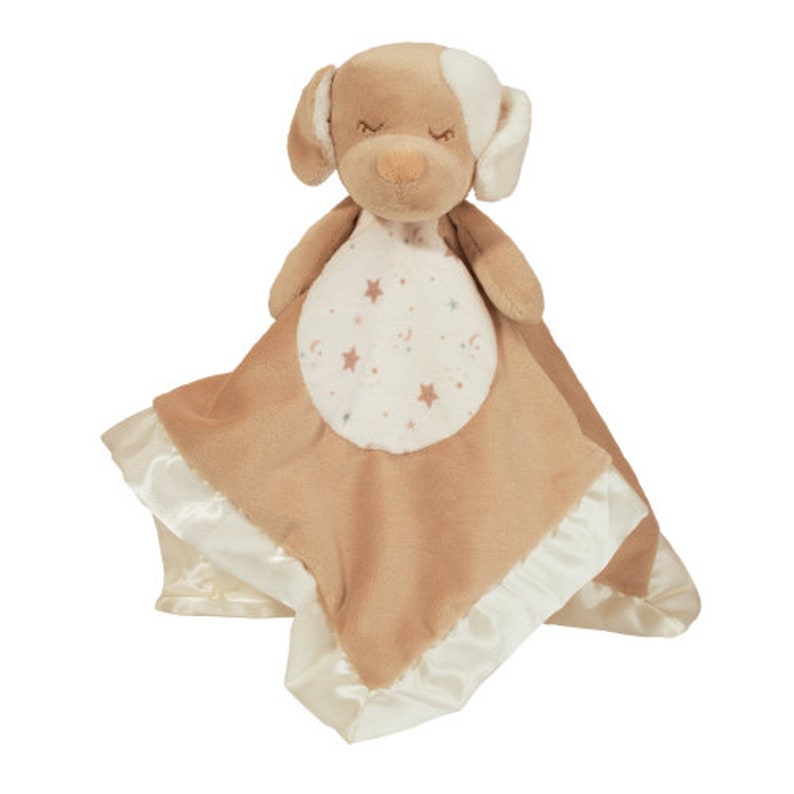 May include: A plush dog-shaped baby security blanket in tan and white. The dog has closed eyes and a white patch on its head. The blanket is tan with a white satin trim and a circular patch with stars and moons.