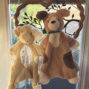 May include: Two plush dog-shaped baby blankets. One is tan with white accents and a star pattern. The other is brown and tan with white accents and a blue collar. Both have floppy ears and are soft to the touch.
