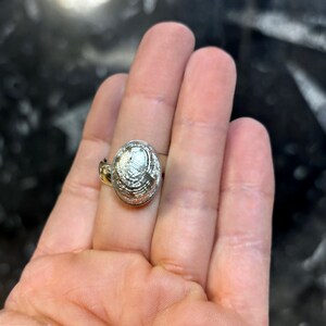 May include: A silver ring with a large oval-shaped stone. The stone has a textured surface that resembles a fingerprint.