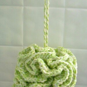 May include: A green and white crocheted bath pouf hanging from a suction cup hook. The pouf is made of soft yarn and is designed for exfoliating and cleansing the skin.
