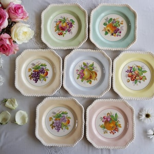 May include: A collection of eight square decorative plates with a fruit design. Each plate has a different pastel color, including green, blue, yellow, and pink. The plates have a rope-like border and a central fruit illustration.