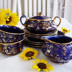 May include: A cobalt blue tea set with gold floral accents. The set includes a teapot, creamer, sugar bowl, and two teacups with saucers.