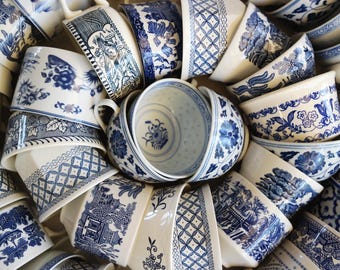 May include: A collection of ceramic bowls and cups featuring a white base with intricate blue transferware patterns, including floral motifs, geometric lattice designs, and landscape scenes, arranged in a circular, overlapping composition.
