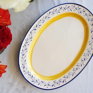 Puede incluir: Una bandeja de servicio ovalada de cerámica con un centro blanco, un borde ancho pintado en amarillo y un borde exterior azul oscuro. El borde está decorado con un delicado patrón de enredadera azul oscuro pintado a mano con hojas y bayas.