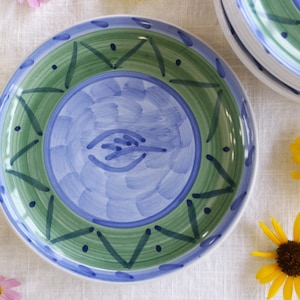 May include: A blue and green ceramic plate with a stylized design. The plate has a blue center with a green and white border.
