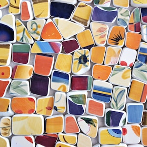 Puede incluir: Primer plano de un mosaico compuesto por baldosas de cerámica de forma irregular. Las baldosas están pintadas con diseños abstractos en tonos amarillos, naranjas, azules y verdes. Cada baldosa está delineada en blanco, creando un efecto de mosaico.