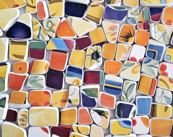 May include: A collection of colorful, irregularly shaped ceramic tiles. The tiles feature a variety of abstract designs in shades of yellow, orange, blue, and green. Each tile is outlined in white, creating a mosaic-like effect.