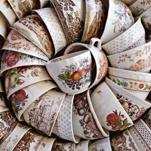 May include: A collection of ceramic bowls and cups arranged in a circular pattern, featuring various brown transferware patterns, floral motifs, and colorful fruit illustrations on cream-colored backgrounds with scalloped and smooth edges.