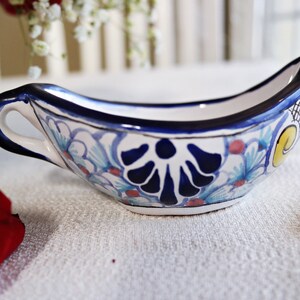 Könnte beinhalten: Eine weiße, gravierte Sauciere mit einem blauen und gelben Blumendesign. Die Sauciere hat einen Griff und ist mit blauer, gelber und roter Farbe verziert.