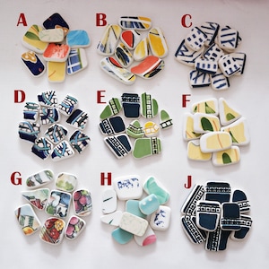 Op de afbeelding: Een verzameling decoratieve keramische tegels in verschillende vormen en maten. De tegels hebben kleurrijke ontwerpen met blauwe, gele, rode en groene accenten. Elke tegel heeft een uniek patroon, waaronder geometrische vormen en abstracte kunst.