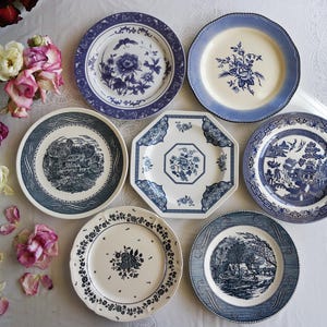 Peut inclure: Une collection d'assiettes en céramique vintage de différentes formes et tailles. Les assiettes présentent des motifs floraux, paysagers et géométriques bleus et blancs. Certaines assiettes ont des bords festonnés. L'arrangement comprend un bouquet de roses roses et blanches.