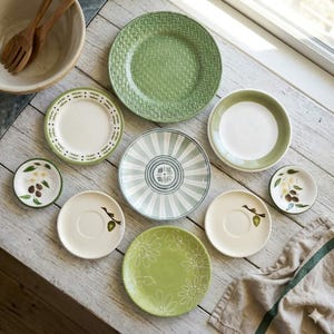 May include: A collection of ceramic tableware including a large green plate with a woven texture, a plate with a green striped pattern, two small plates with olive branch illustrations, two saucers with olive motifs, and a green floral plate.