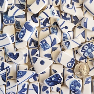 May include: A collection of white ceramic tiles with blue floral patterns. The tiles are various shapes and sizes, and some have a slightly textured surface.