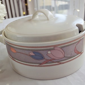 Könnte beinhalten: Weiße Keramik-Servierplatte mit Deckel. Die Platte hat ein florales Design mit rosa, blauen und orangefarbenen Blumen auf einem violetten Hintergrund.