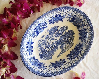 May include: A white oval serving dish with a blue and white floral pattern. The dish features a central design of a blue and white castle with trees and a river.