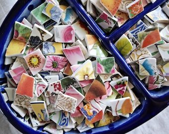 May include: A blue ceramic bowl divided into three sections, filled with colorful, broken pieces of china. The pieces are various shapes and sizes, with floral and geometric patterns.
