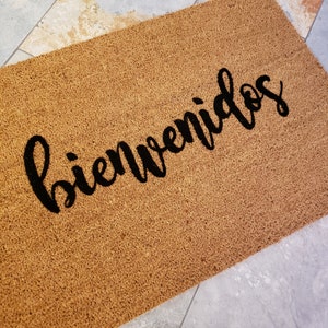 以下が含まれることがあります： 黒い筆記体で「Bienvenidos」と書かれた茶色のココナッツ繊維のドアマットです。