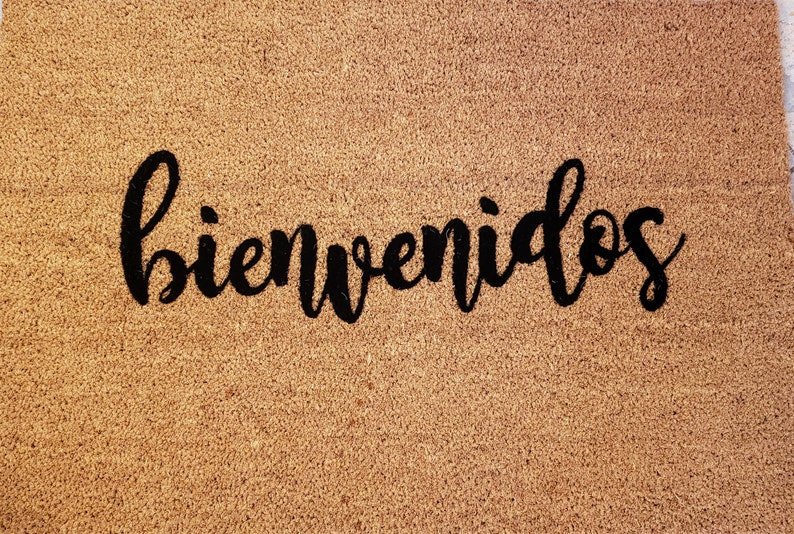 以下が含まれることがあります： 黒い筆記体で「bienvenidos」と書かれた茶色のココナッツ繊維のドアマットです。