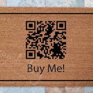 May include: A brown doormat with a black border and a black QR code in the center. The text "Buy Me!" is printed below the QR code.