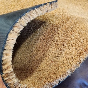 K&ouml;nnte beinhalten: Nahaufnahme einer braunen Kokosmatte mit schwarzem Gummiboden. Die Matte ist in der Mitte gefaltet und zeigt die Textur der Kokosfasern.