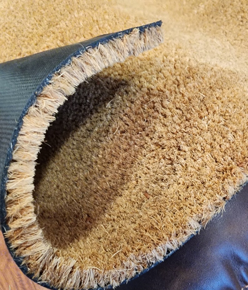 K&ouml;nnte beinhalten: Nahaufnahme einer braunen Kokosmatte mit schwarzem Gummiboden. Die Matte ist in der Mitte gefaltet und zeigt die Textur der Kokosfasern.