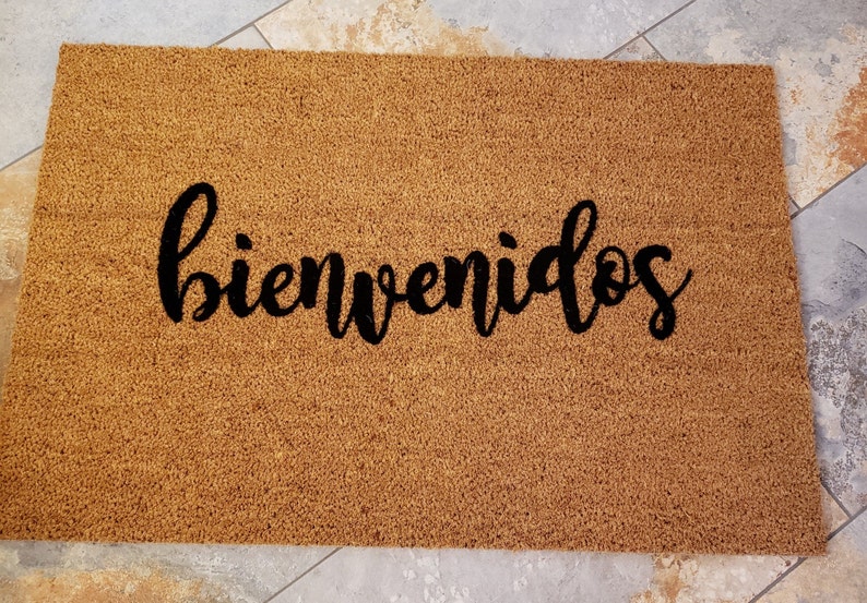 以下が含まれることがあります： 黒い筆記体で「bienvenidos」と書かれた茶色のココナッツ繊維のドアマットです。