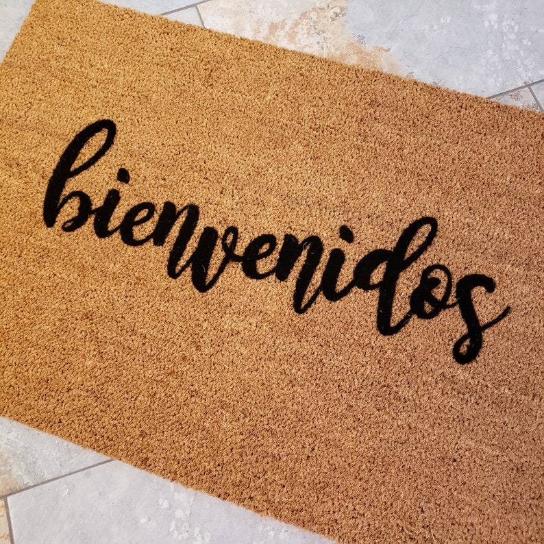 以下が含まれることがあります： 黒い筆記体で「bienvenidos」と書かれた茶色のココナッツ繊維のドアマットです。