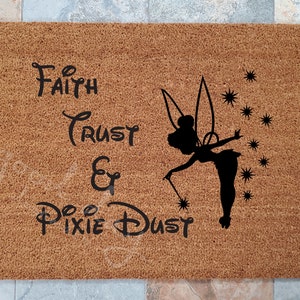 May include: A brown coir doormat with the text "To Faith Trust & Pixie Dust" and a black silhouette of Tinkerbell with her wand and pixie dust.