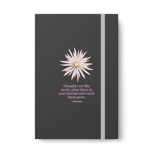May include: A dark gray journal with a white flower illustration and the quote "Thoughts are like seeds; plant them in your journal and watch them grow. - Unknown".