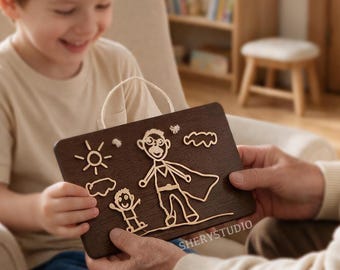 Puede incluir: Una placa rectangular de madera marrón oscuro con un diseño de líneas en relieve de color claro que muestra una figura de superhéroe junto a un niño pequeño, con un sol y nubes de fondo. El texto SHERYSTUDIO es visible en la esquina inferior.