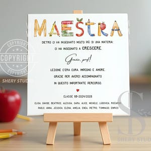 Può includere: Una stampa su tela bianca su un piccolo cavalletto di legno. La stampa presenta la parola "MAESTRA" in lettere colorate, insieme a testo in italiano. Una mela rossa e delle matite sono visibili sullo sfondo. L'indirizzo del sito web "WWW.SHERYSTUDIO.COM" è in alto.