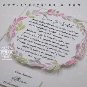 Puede incluir: Una tarjeta blanca con un borde de corona floral y un mensaje escrito a mano en tinta negra. El mensaje dice "Cara Zia Isabel Sono felice che tu sia la mia madrina. Prenderai le mie piccole mani e le terrai tra le tue insegnandomi la giusta via, l'amore e il rispetto. Mi incoraggerai e sarai il mio dono per la vita. La tua amorevole guida, il tuo sostegno e le tue preghiere sono il pi&ugrave; grande tesoro che potessi ricevere. Ti ringrazio per essere qui nel giorno del mio Santo Battesimo. La tua presenza &egrave; il pi&ugrave; grande dei regali. Con Amore Athena 29 dicembre"