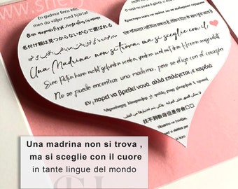 Może przedstawiać: Biała karta w kształcie serca z tekstem "Una madrina non si trova, ma si sceglie con il cuore in tante lingue del mondo" w kolorze czarnym. Karta znajduje się na różowym tle.