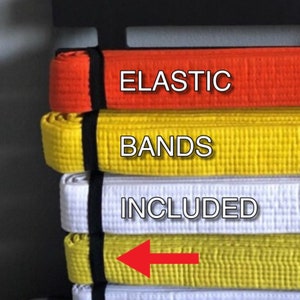 May include: A black belt rack with multiple colored belts hanging on it. The belts are held in place by elastic bands. The text "ELASTIC BANDS INCLUDED" is visible on the image.
