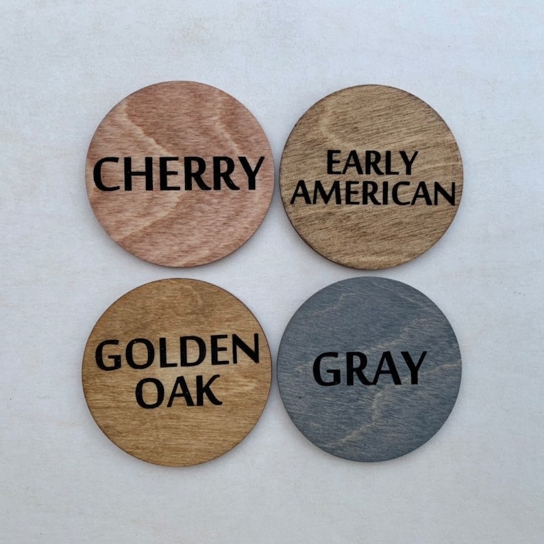 May include: Four wooden circles with different wood stains. The stains are labeled "Cherry", "Early American", "Golden Oak", and "Gray".